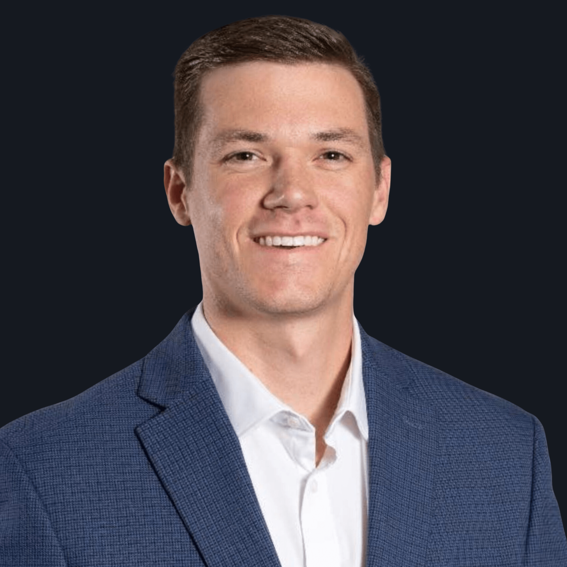 A smiling man in a blue textured suit jacket and white dress shirt poses in front of a plain dark background.